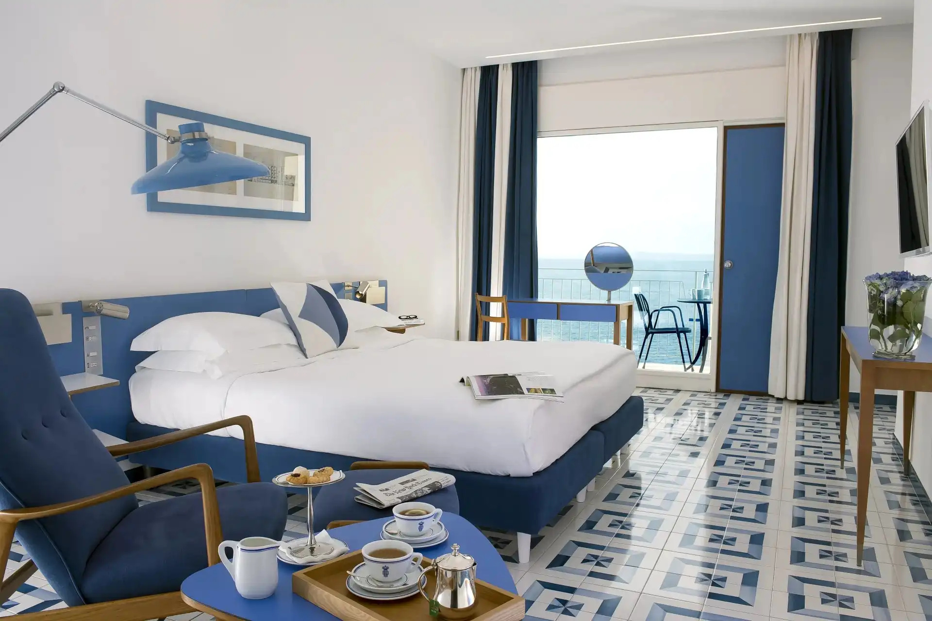 Elegant hotel room with blue and white decor, featuring sea view balcony and contemporary Italian design