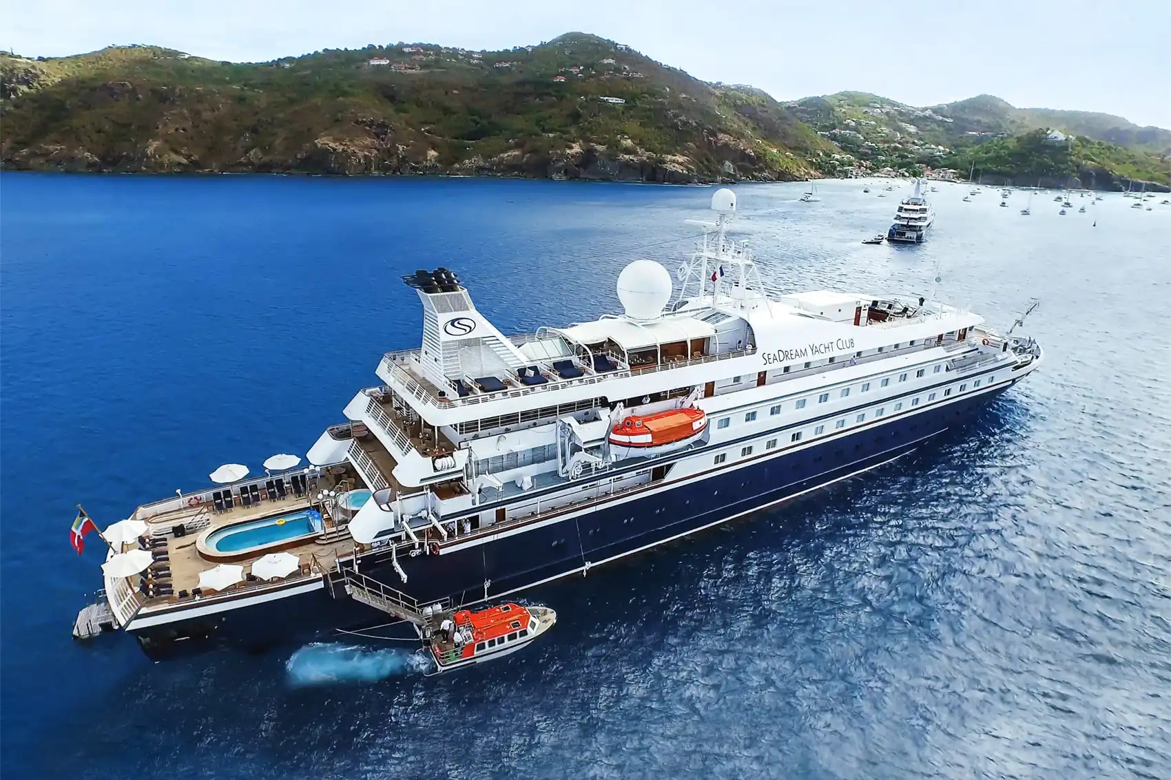 Luxury cruise ship anchored in crystal blue waters near a green mountainous coastline
